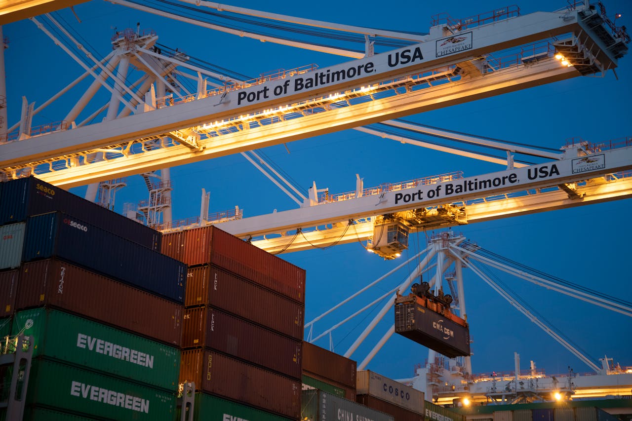 why-choose-us Illuminated cargo cranes at the Port of Baltimore with stacked containers at dusk.