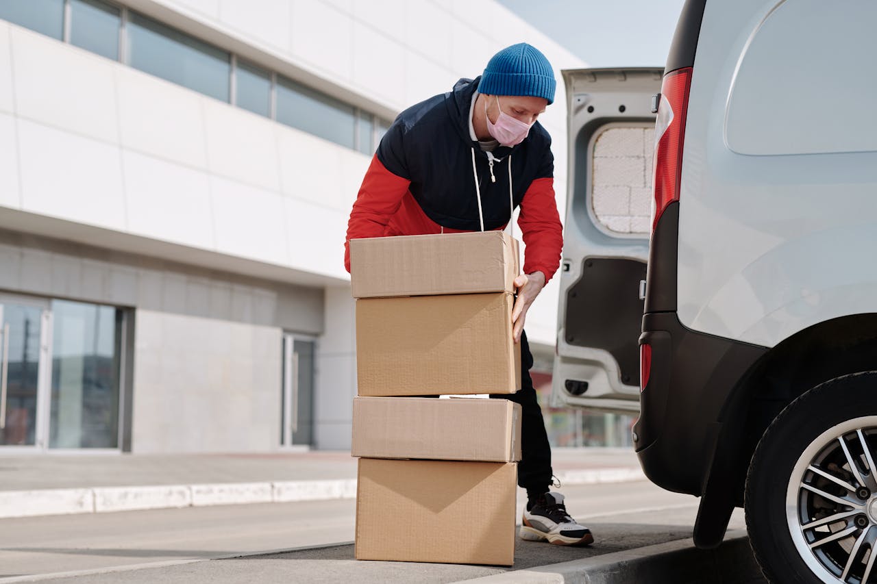 brand-03 Delivery worker wearing a face mask loads boxes into a van, reflecting pandemic precautions.