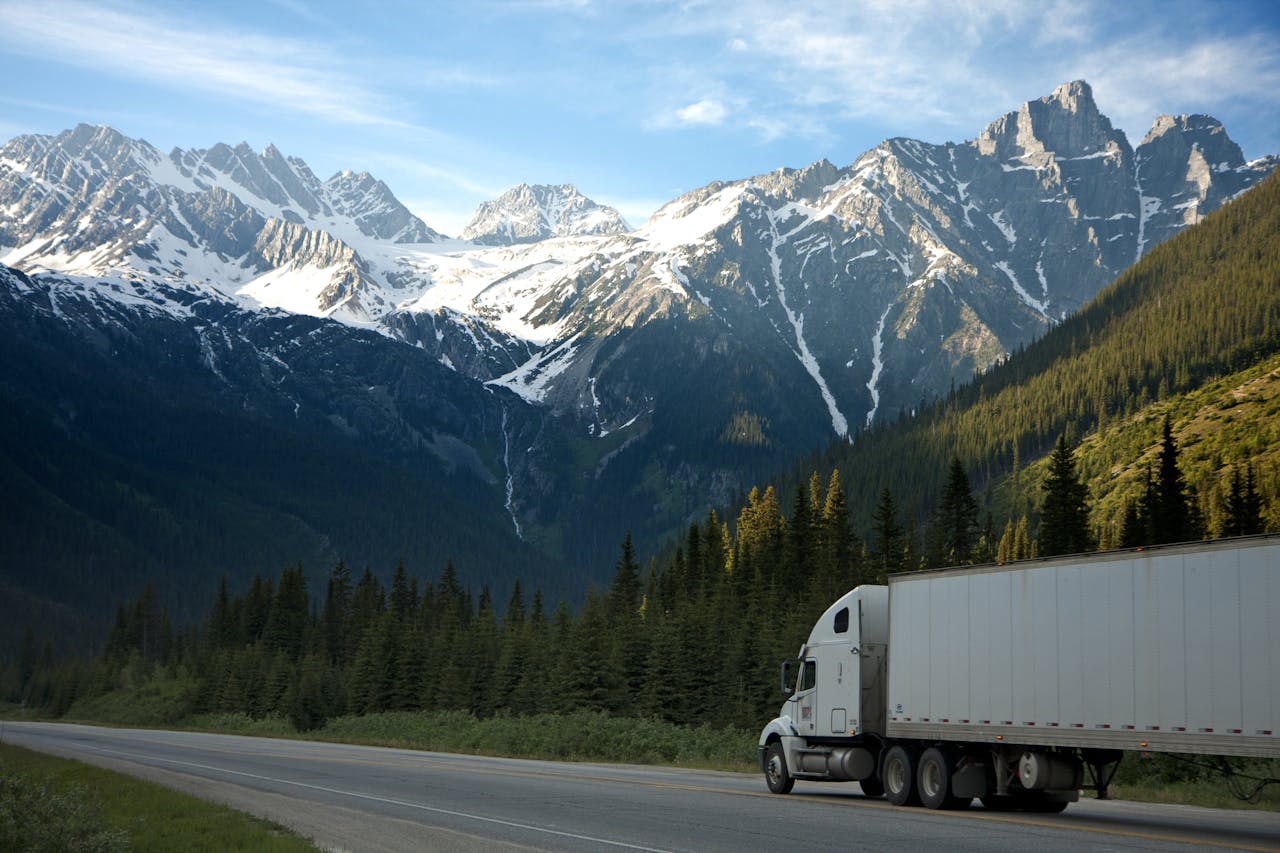 digital A semi-truck travels along a highway with snow-capped mountains in the background.
